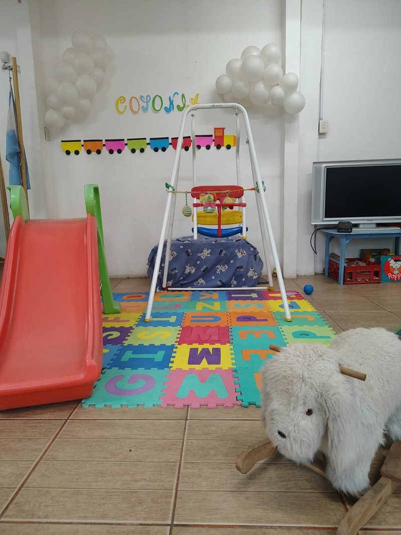 Rincón de juego de la sala con tobogán, hamaca, alfombra de goma eva con letras y un caballito de peluche